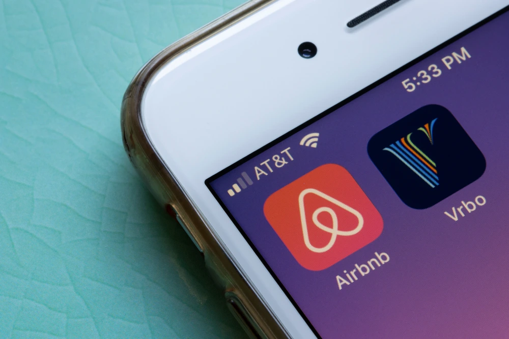 Alt text: "Close-up of a smartphone screen displaying the Airbnb and Vrbo app icons with a notification bar showing the AT&T network, Wi-Fi signal, and the time as 5:33 PM.
